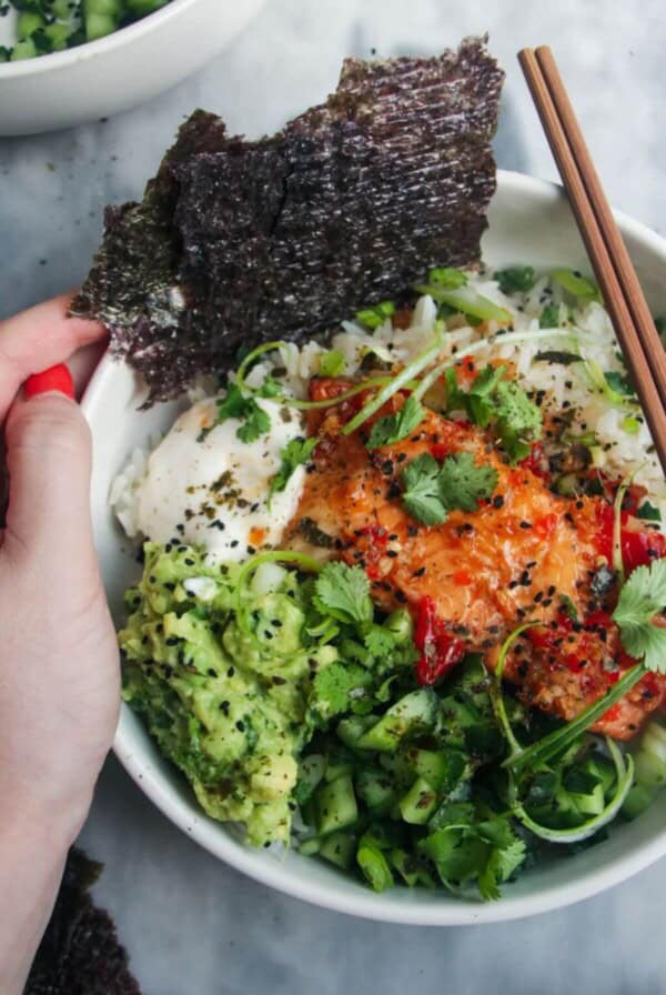 Hand holding a loaded salmon sushi rice bowl.