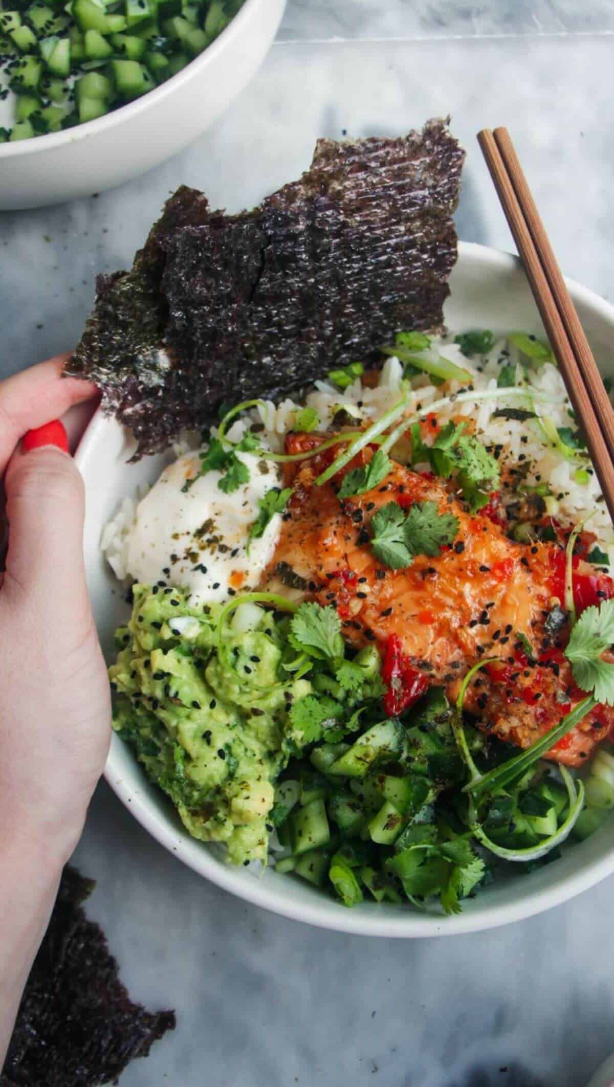 Hand holding a loaded salmon sushi rice bowl.