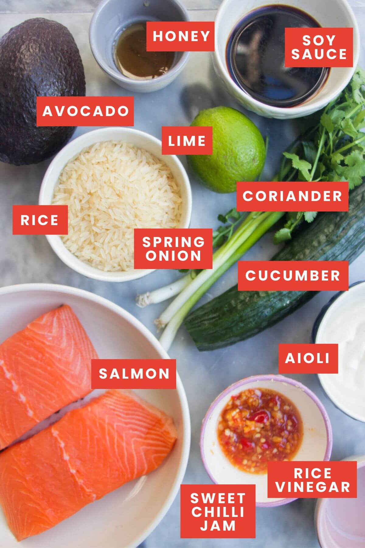 Ingredients for salmon sushi rice bowls laid out on a grey marble background and labelled.