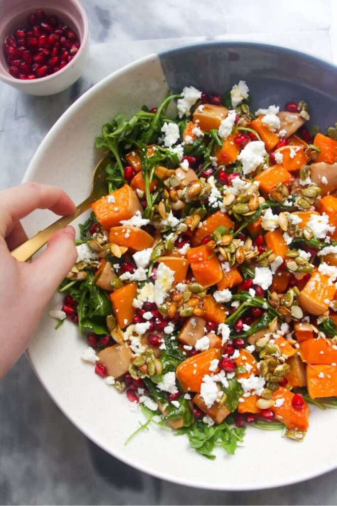 Hand holding a gold spoon, stirring colourful butternut squash salad.