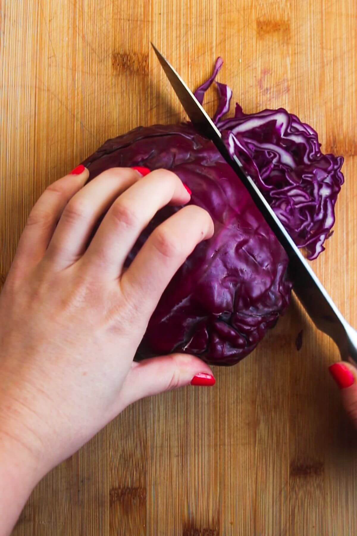 Hand holding red cabbage and slicing it thinly with a large knife.
