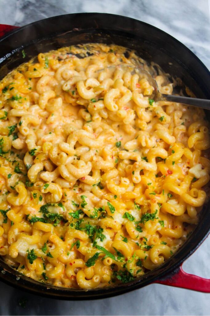 Spicy mac and cheese in a large black skillet with a serving spoon inside.