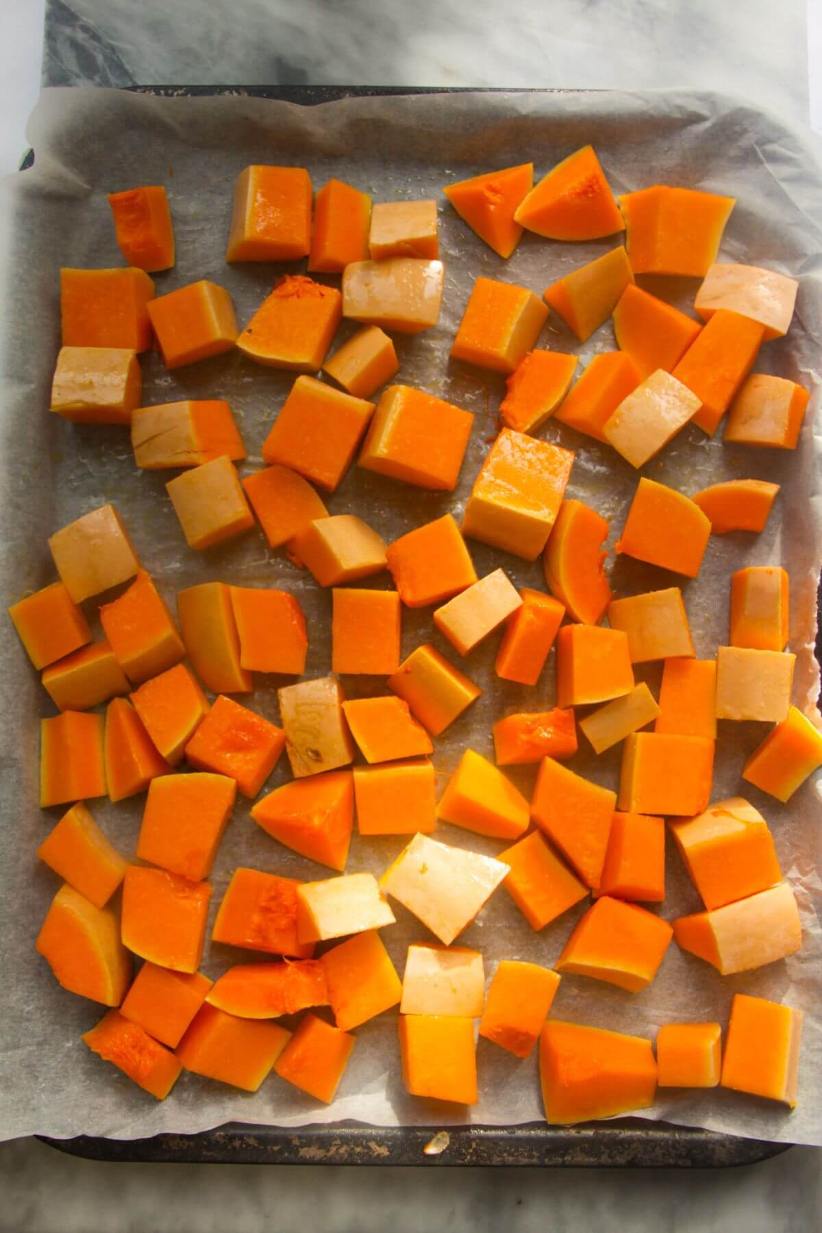 Butternut squash cubes on a lined oven tray.