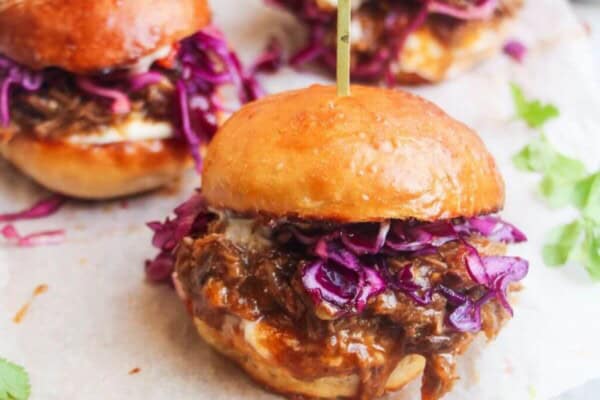3 pulled pork sliders on a small wooden board.