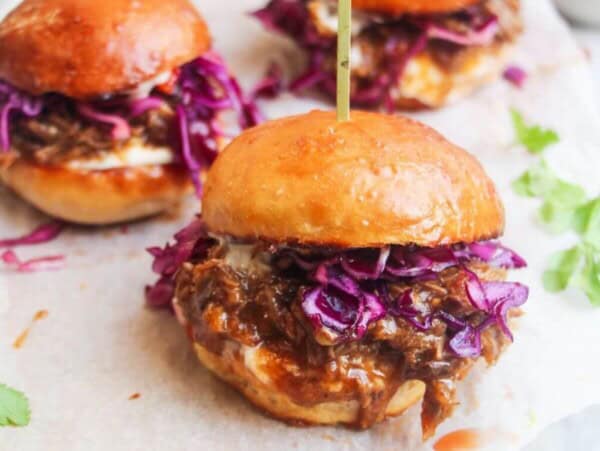 3 pulled pork sliders on a small wooden board.