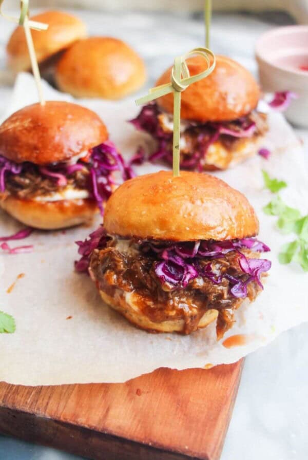 3 pulled pork sliders on a small wooden board.
