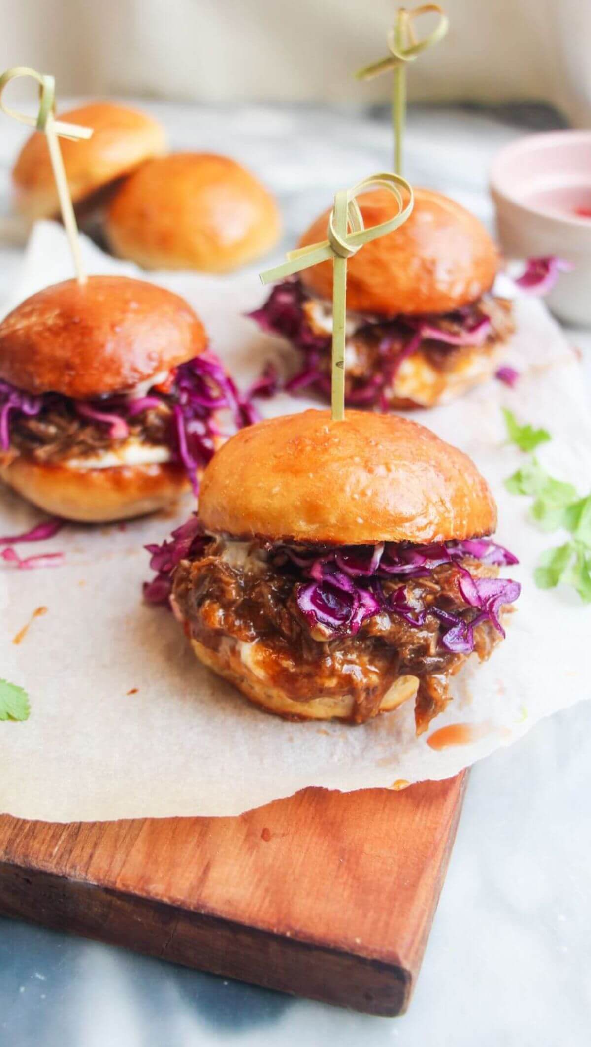 3 pulled pork sliders on a small wooden board.