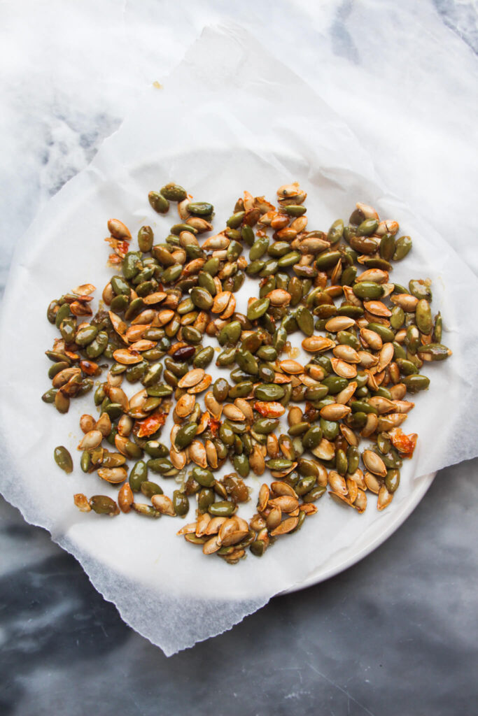 Sticky pumpkin seeds on a baking paper lined white plate.