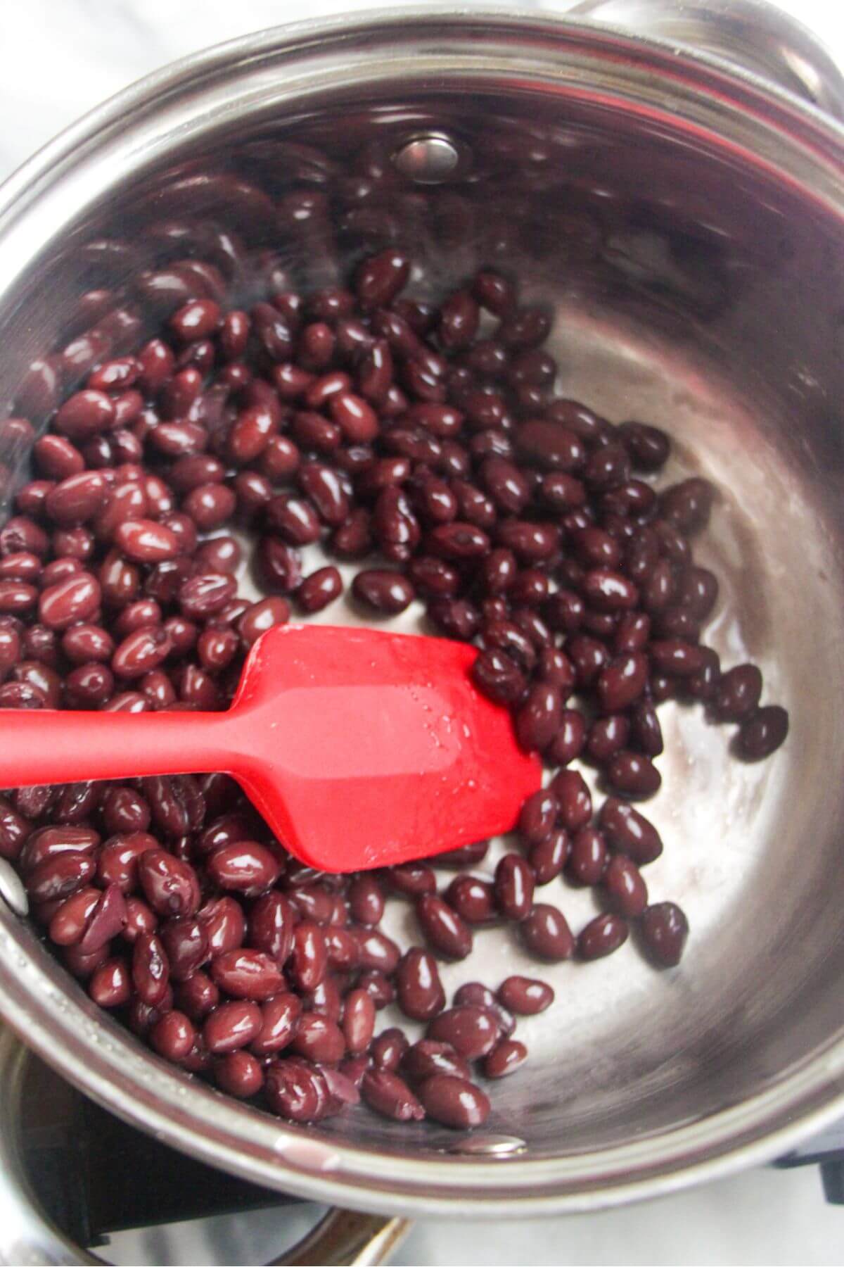 Small red spatula stirring black beans in a small silver pot.
