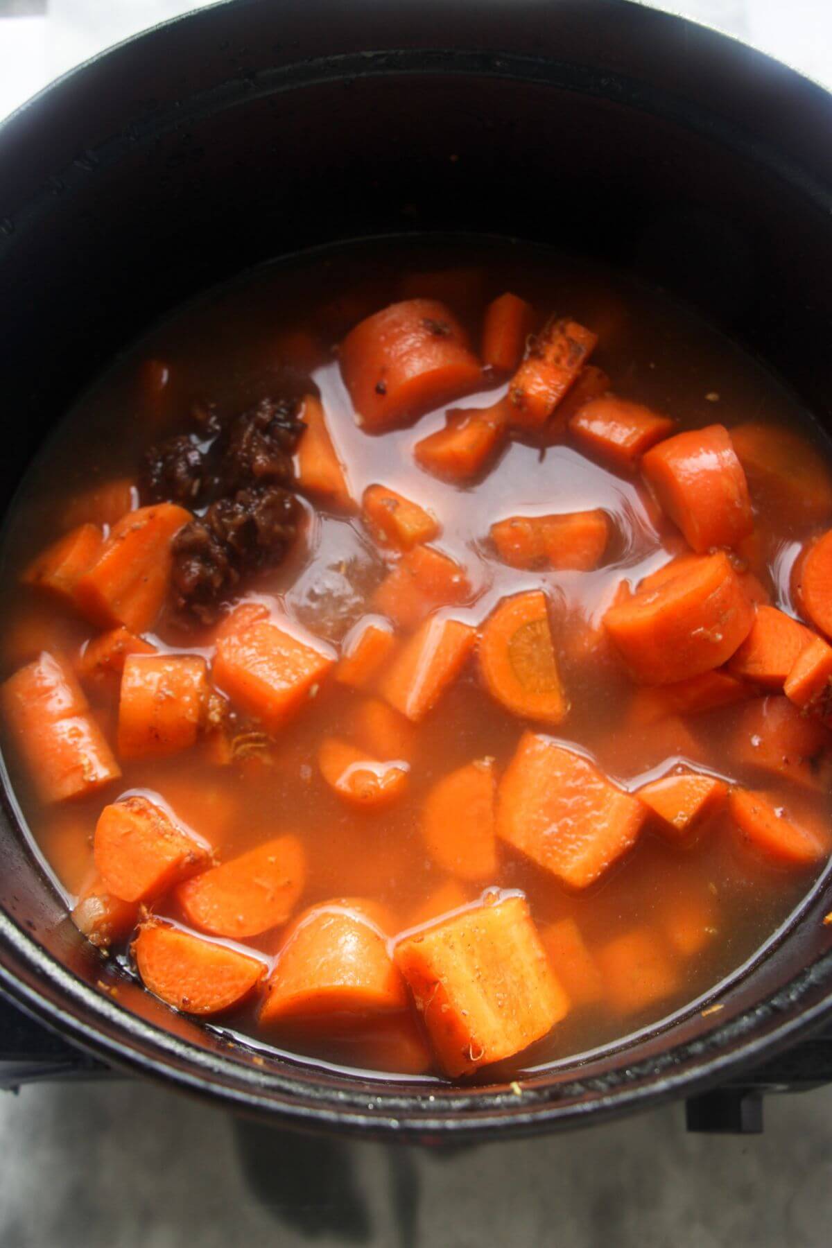 Stock added to a large black pot with chopped carrots in it.