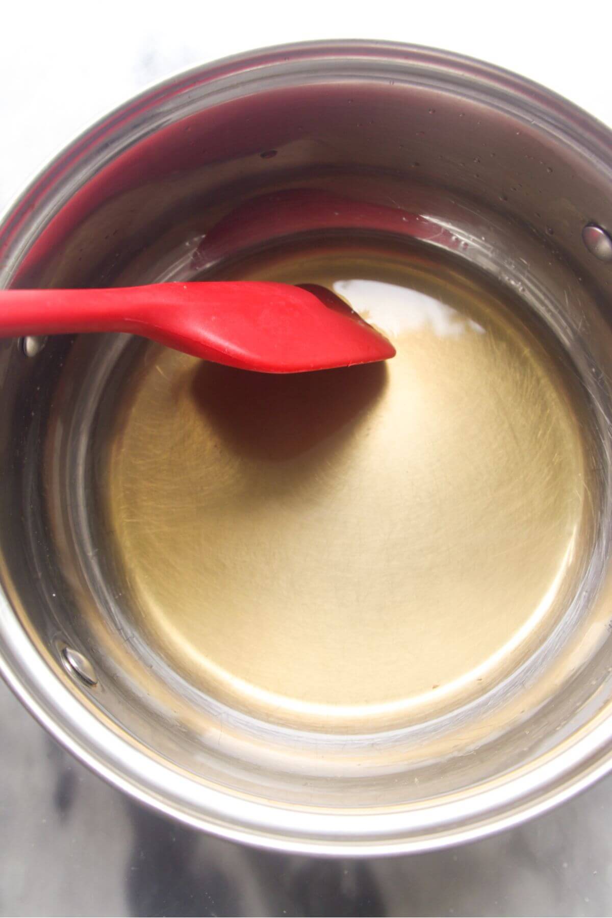 Small red spatula stirring sugar syrup in a small silver pot.