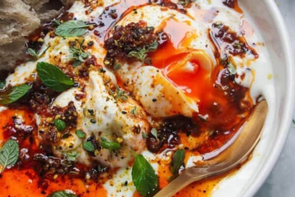Poached eggs with chilli oil and garlick yogurt in a small white bowl with toast on the side.