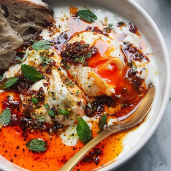 Poached eggs with chilli oil and garlick yogurt in a small white bowl with toast on the side.