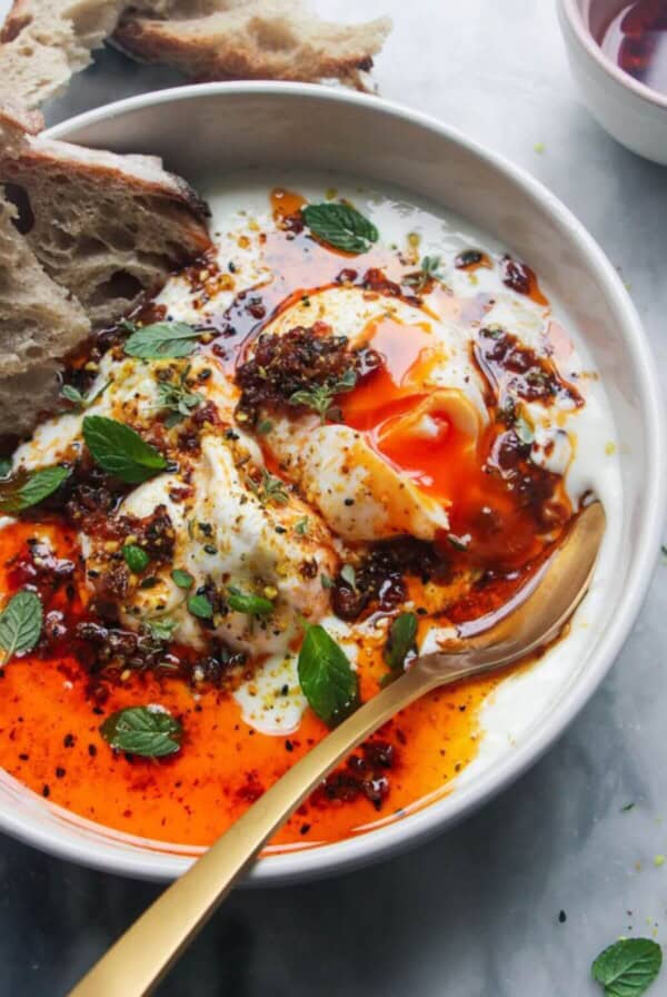 Poached eggs with chilli oil and garlick yogurt in a small white bowl with toast on the side.