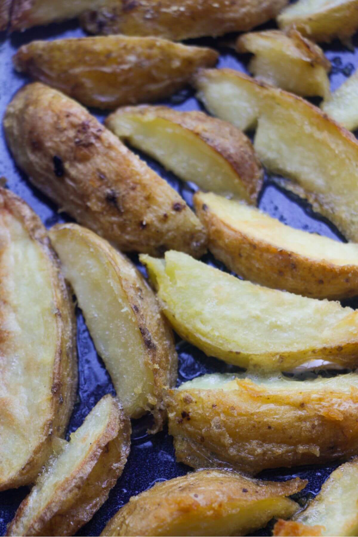 Close up of crispy potato wedges in a blue oven tray.