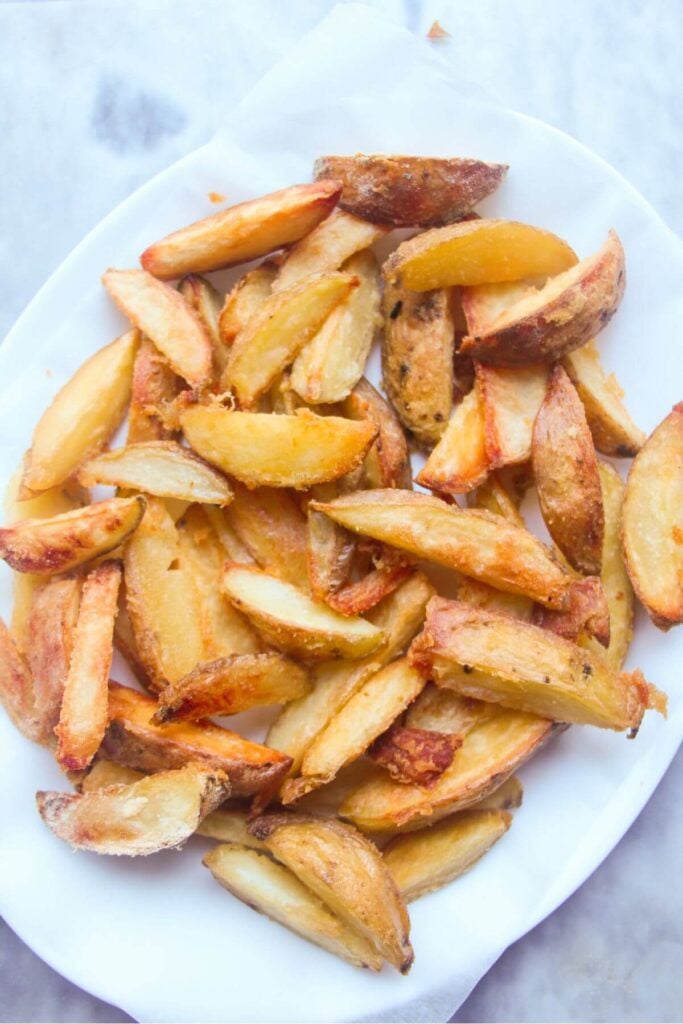 Golden crispy potato wedges on a large white oval plate.