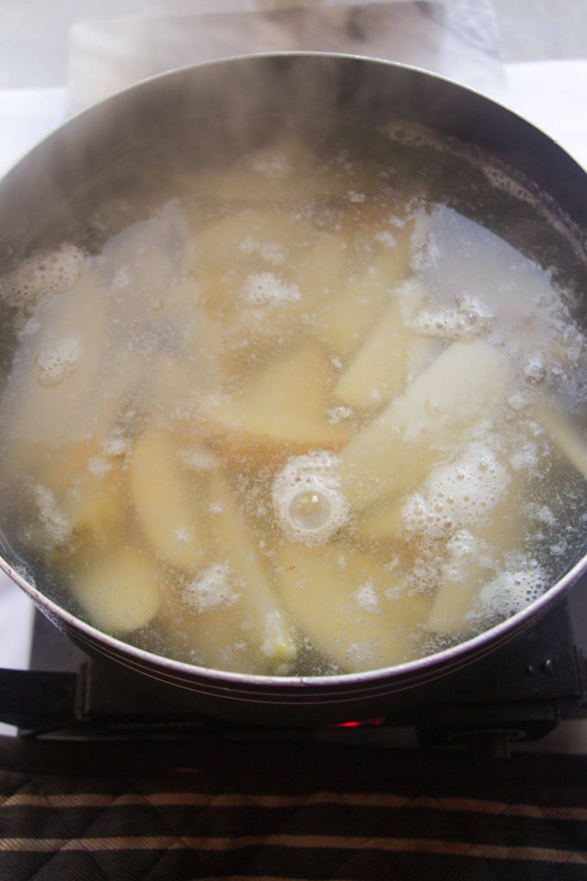 Chopped potato wedges simmering in a large black pot.