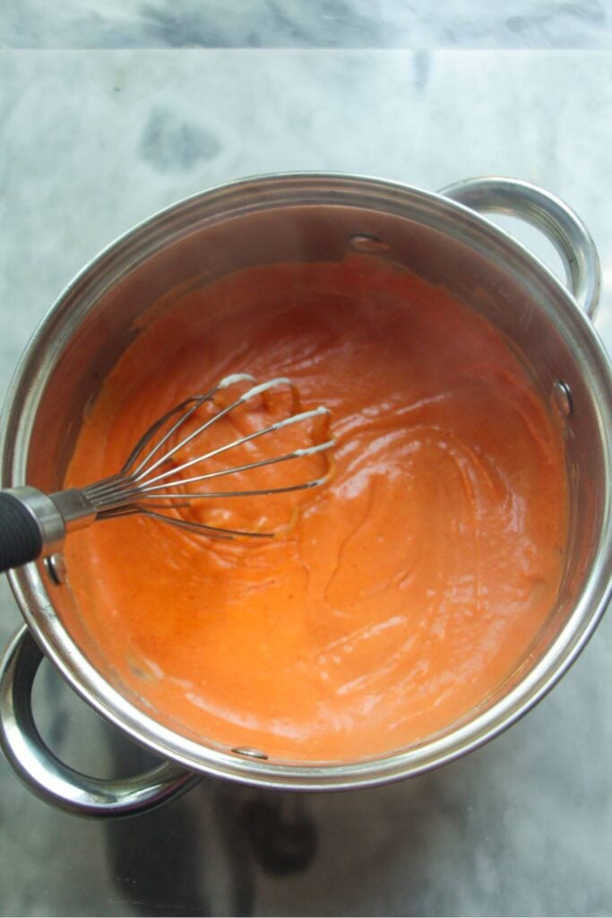 Whisking orange gochujang bechamel in a small silver pot.