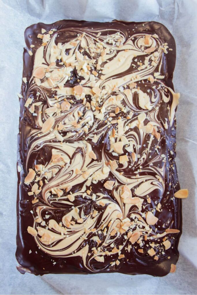 Flaked almonds on top of dark and white marbled chocolate in a lined oven tray.