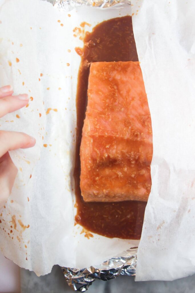Hand wrapping maple miso glazed salmon fillet in baking paper.