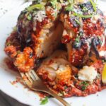 Whole roasted cauliflower with a slice cut out of it, with a fork piercing a piece of cauliflower.