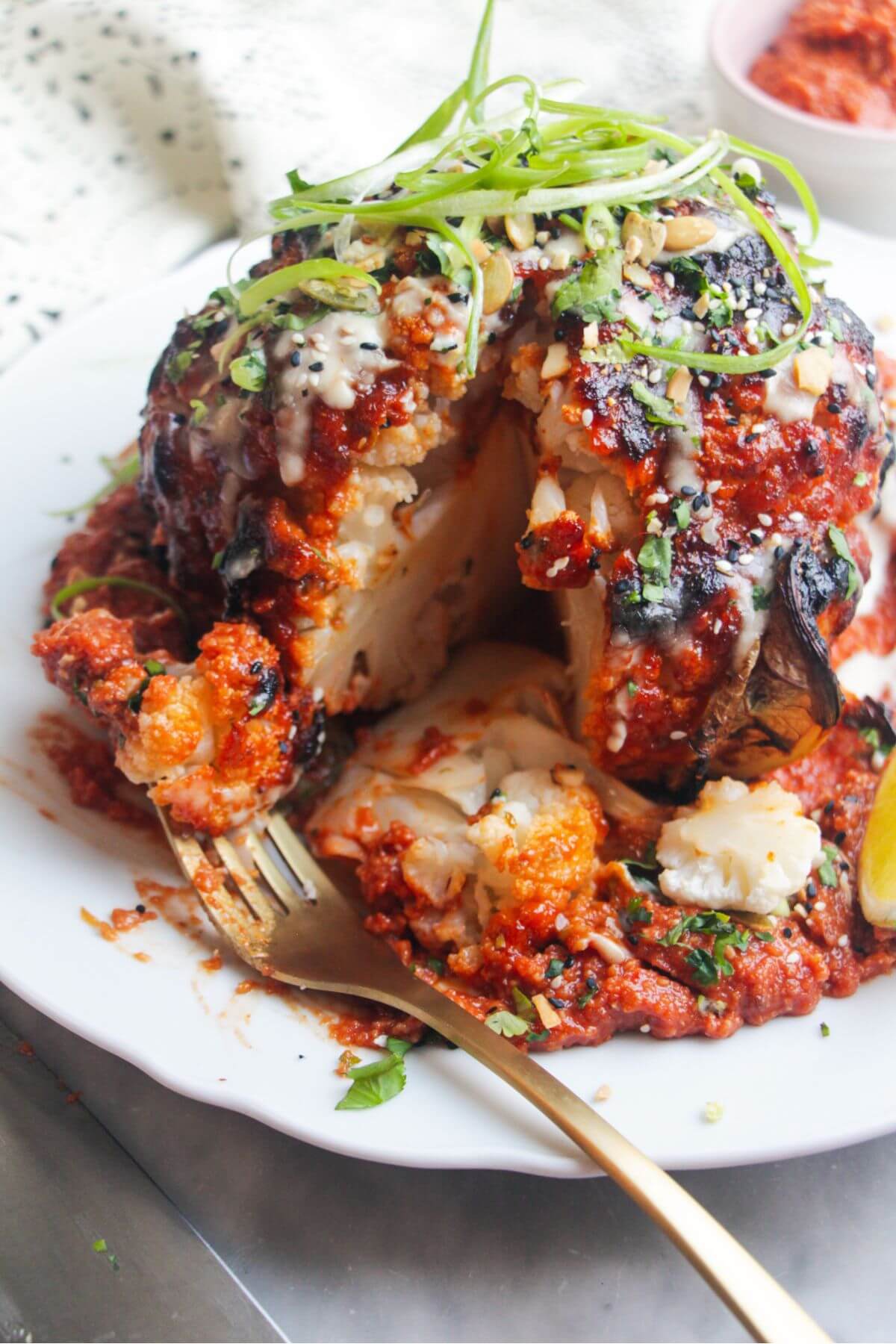 Whole roasted cauliflower with a slice cut out of it, with a fork piercing a piece of cauliflower.
