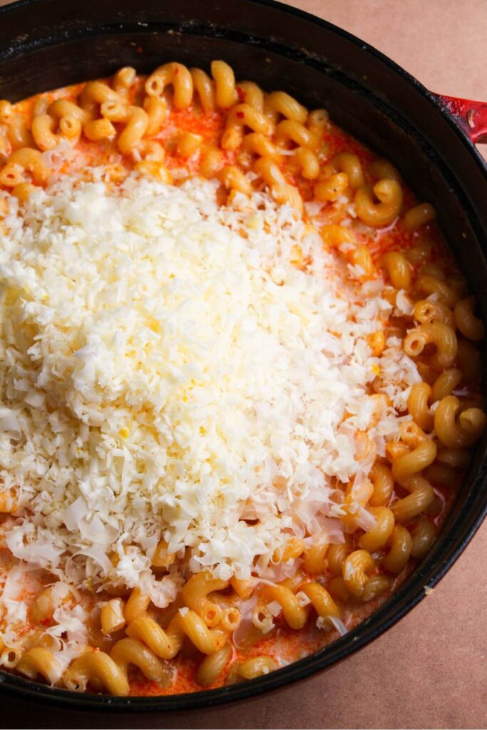 Grated cheese piled on top of macaroni in a large black skillet.