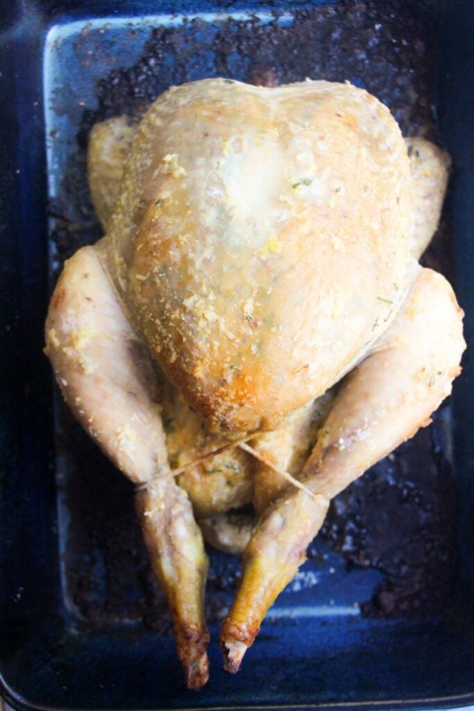 Whole chicken after being roasted under foil for an hour, in a blue oven dish.