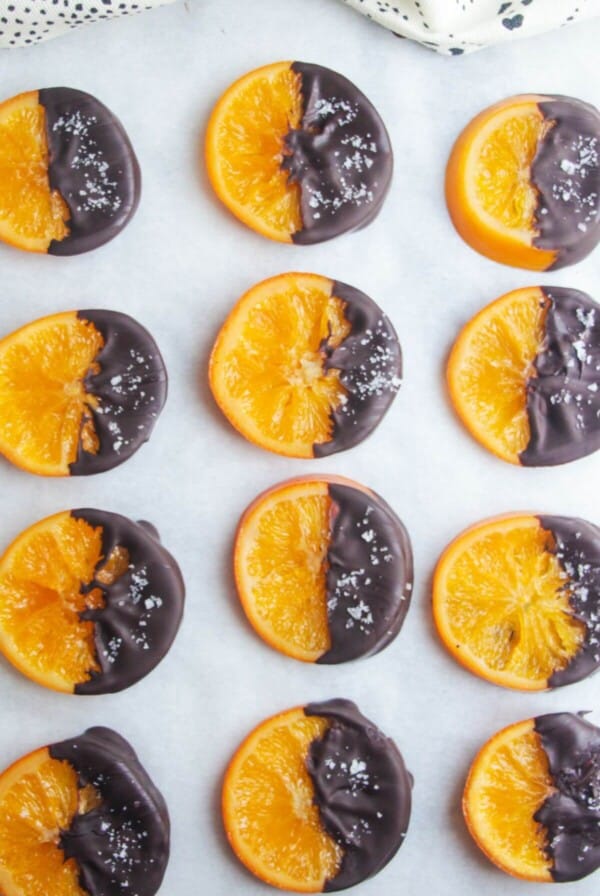 Dark chocolate dipped candied orange slices laid out on a baking paper lined tray.