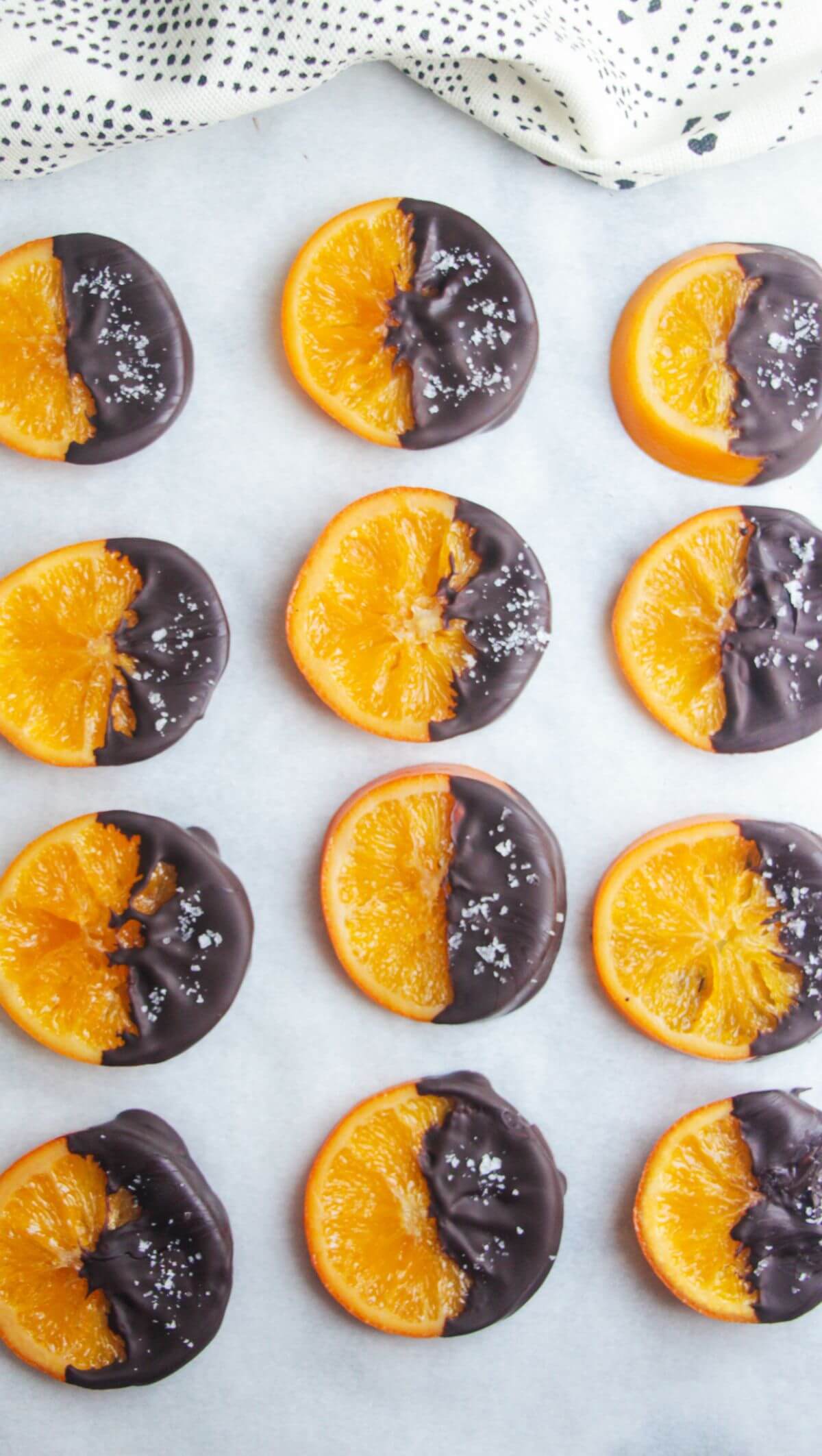 Dark chocolate dipped candied orange slices laid out on a baking paper lined tray.
