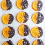 Dark chocolate dipped candied orange slices laid out on a baking paper lined tray.