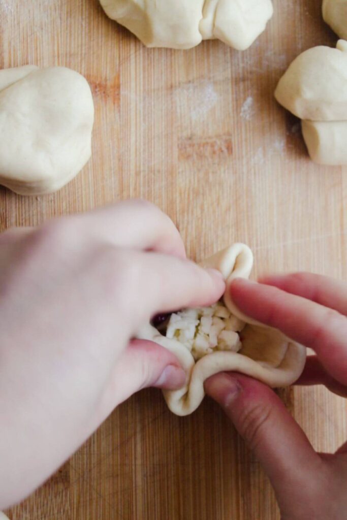 2 hands pinching dough ball together on a wooden board.