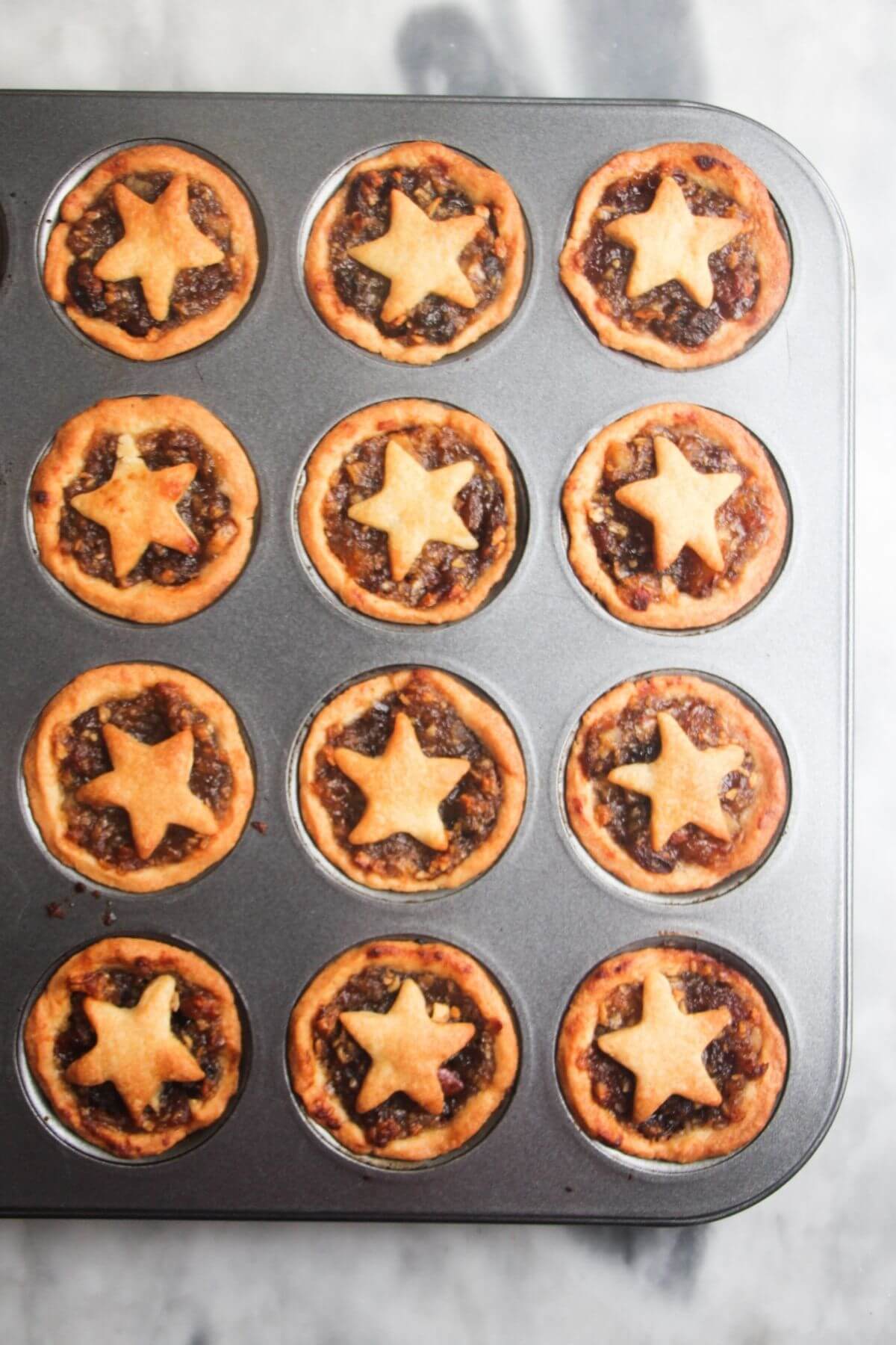 12 cooked, star topped fruit mince pies in mini muffin tin.