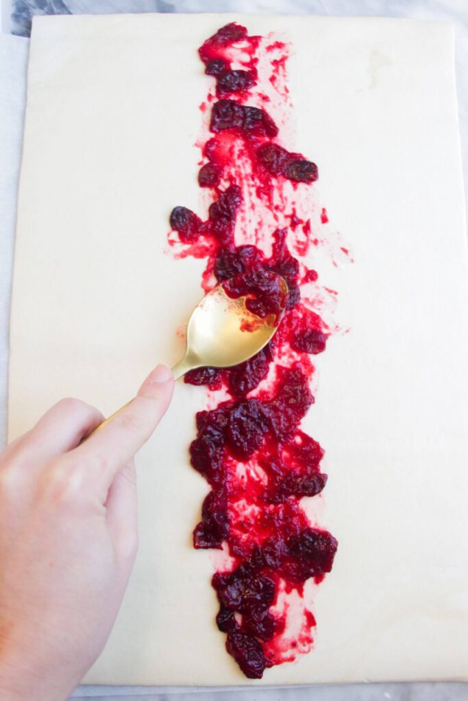 Spooing cranberry sauce down the middle of a puff pastry sheet.