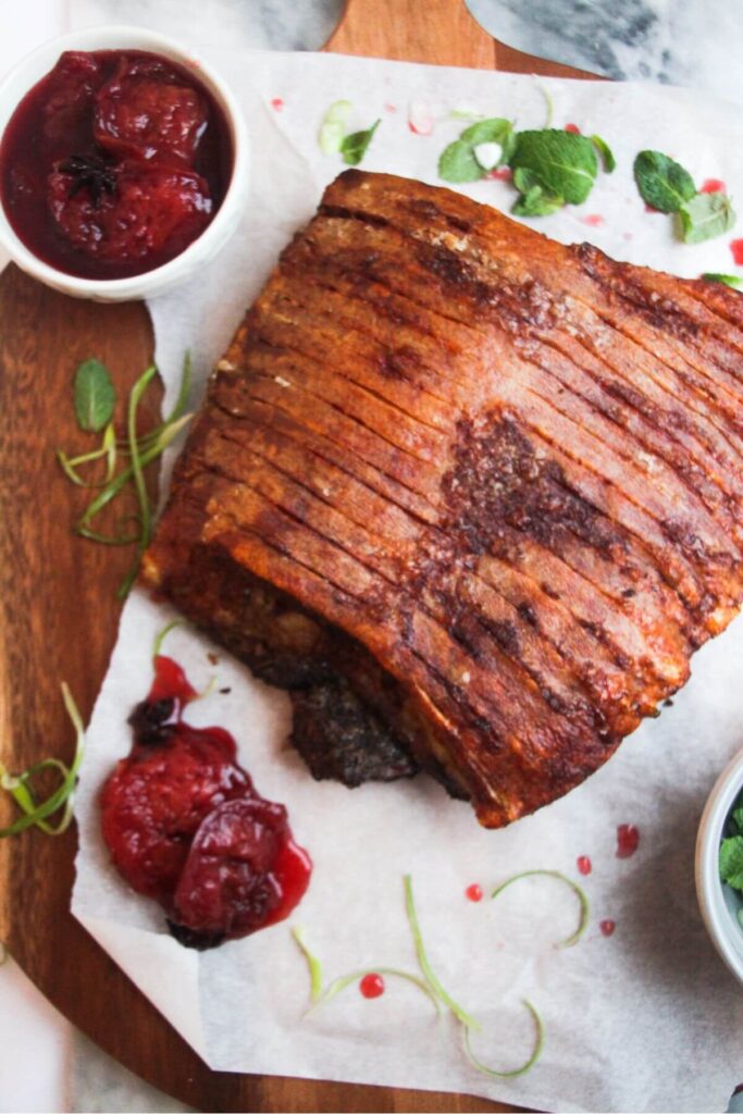 Large piece of crispy pork belly on a wooden serving board, with plum sauce on the side.