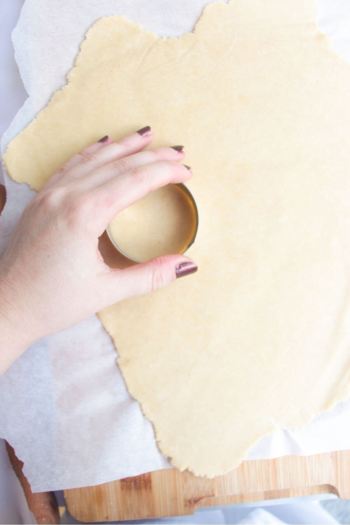 Hand using a small cookie cutter to cut out circles of pastry.