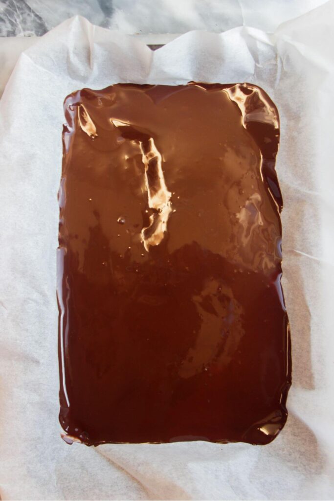 Melted dark chocolate spread out on a baking paper lined tray.