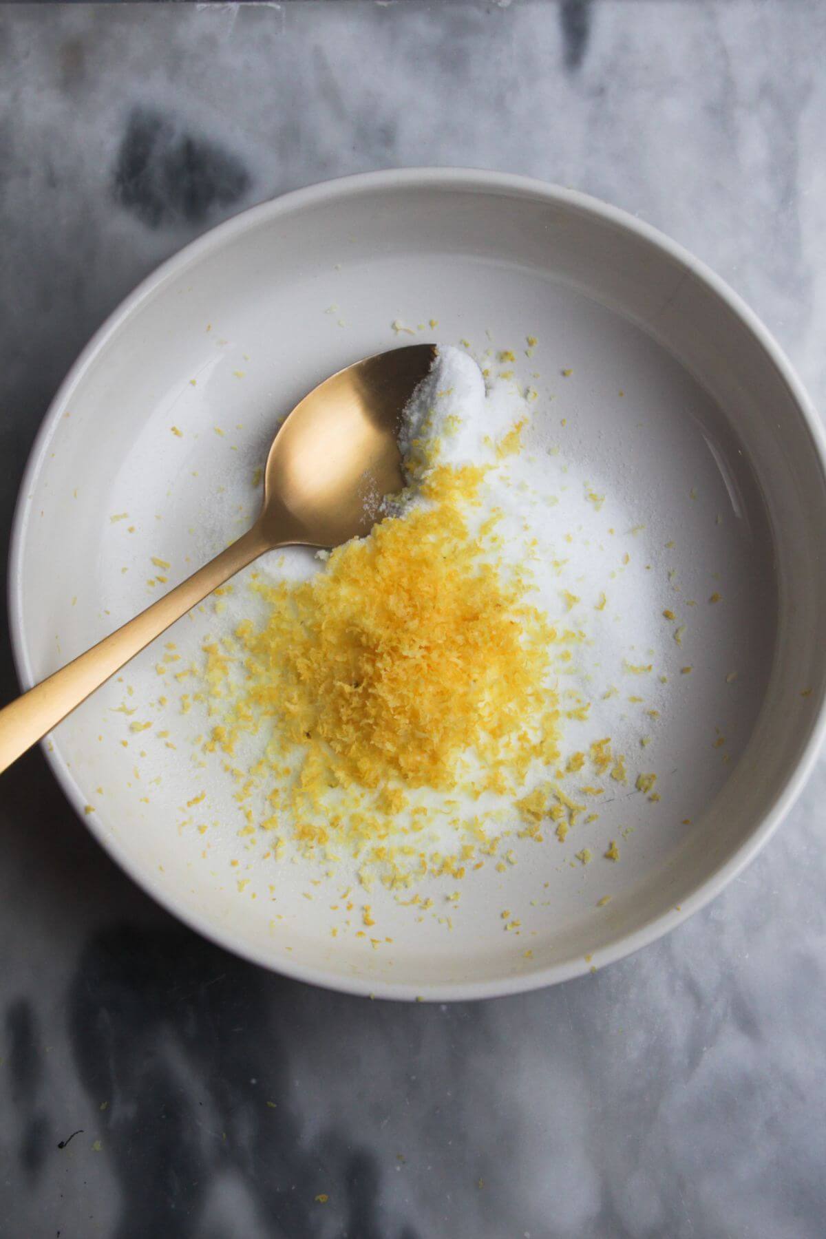 Salt and lemon zest in a small white bowl on a grey marble background.