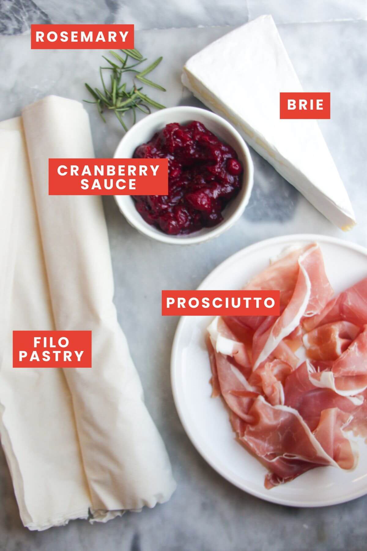 Ingredients for brie, cranberry and prosciutto filo bites laid out on a grey marble background and labelled.