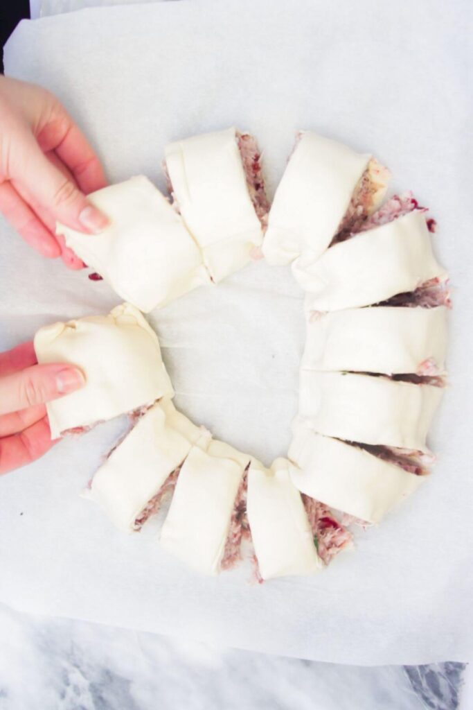 Hands forming sliced sausage roll log into a wreath.
