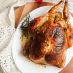 Close up view of golden brown roasted chicken on a white oval plat.