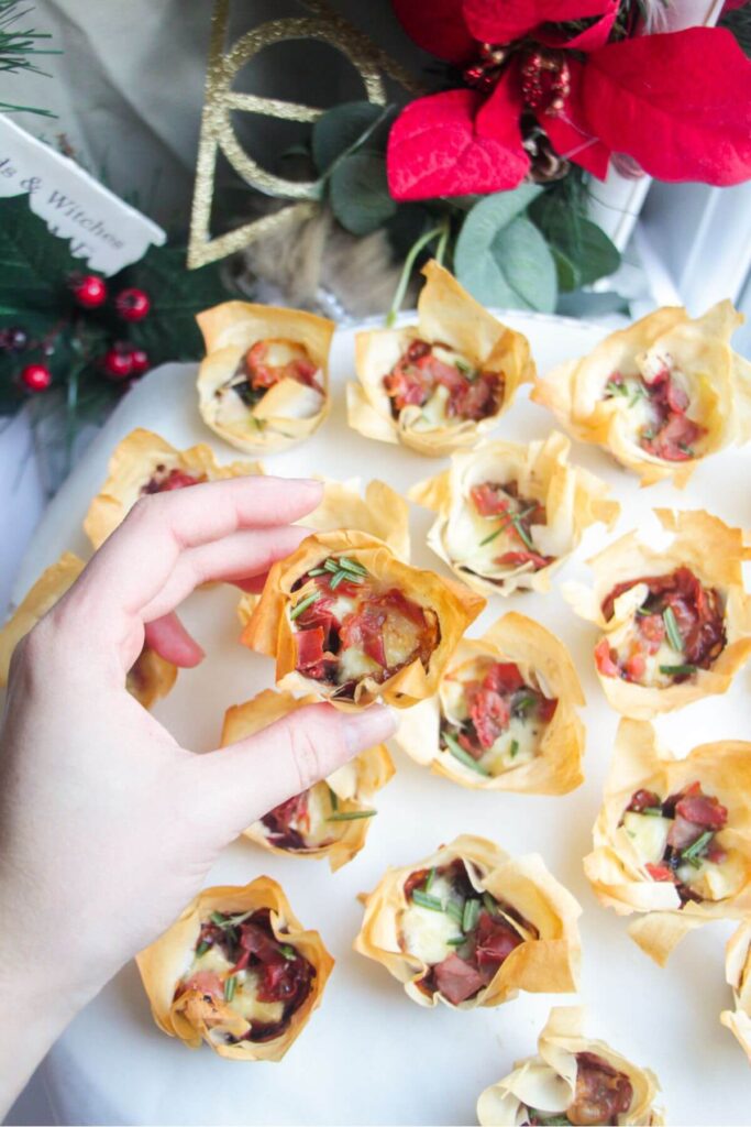 A hand holding up a crispy filo bite with more filo bites in the background.