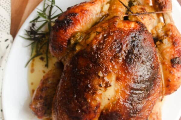 Juicy herb roasted chicken on a white oval plate.
