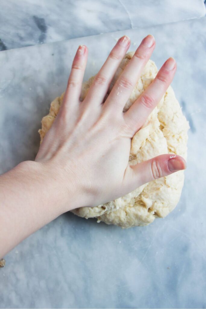 A hand kneading ball of dough on a grey marble background.