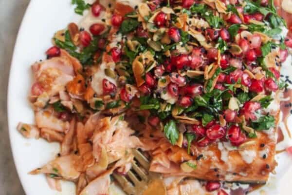 Maple miso glazed salmon fillet with pomegranate almond salsa, with lemon wedges on the side.