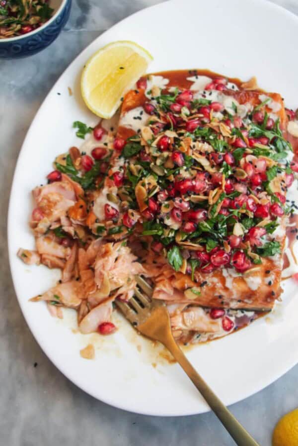Maple miso glazed salmon fillet with pomegranate almond salsa, with lemon wedges on the side.