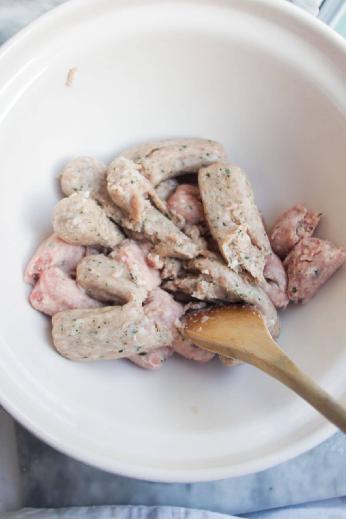 Sausage meat in a large white mixing bowl with a large wooden spoon.