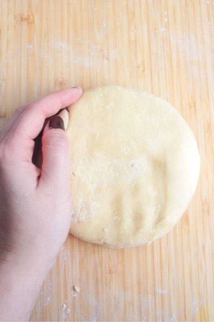 Hand forming a pastry circle on a wooden background.