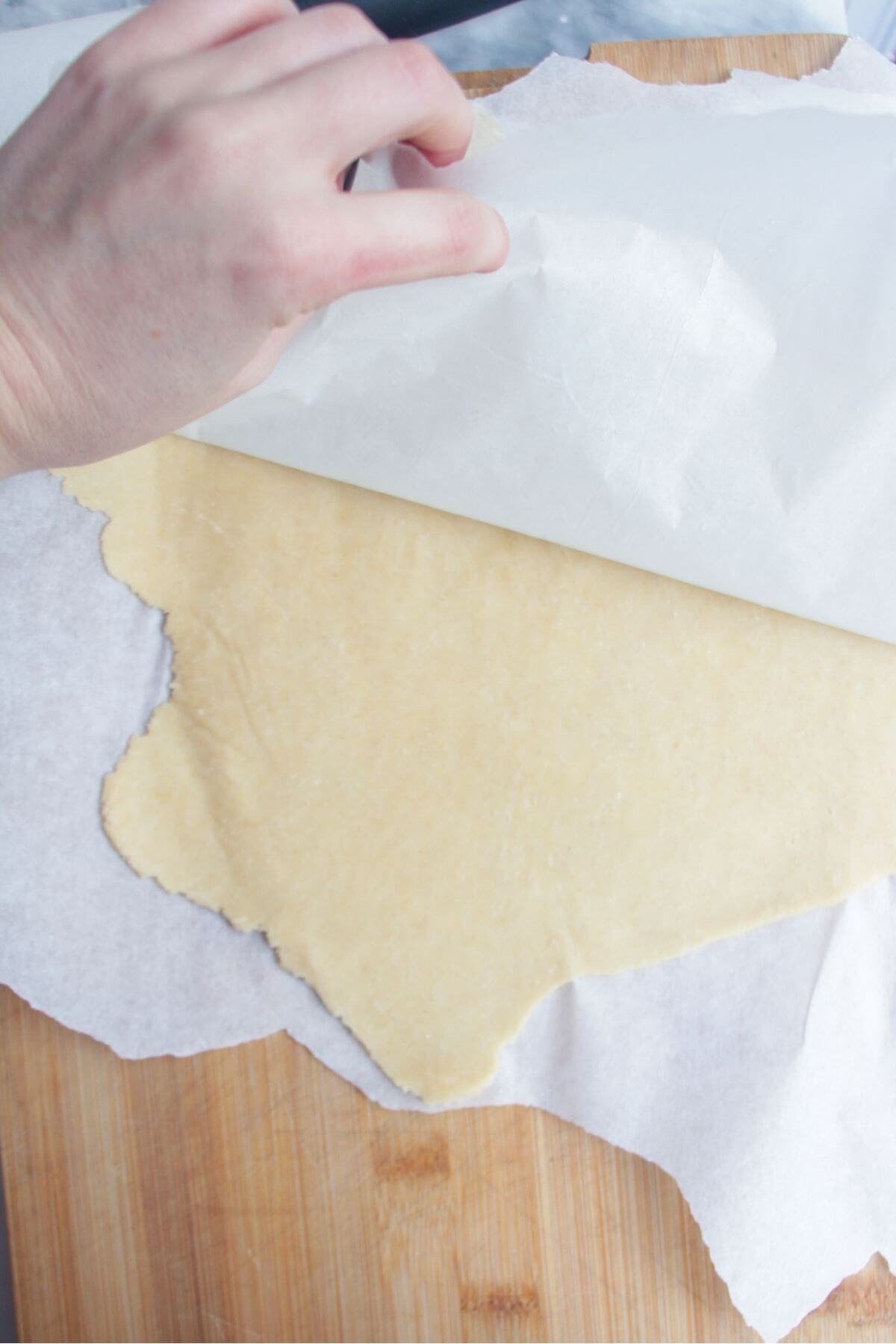 Hand peeling back baking paper to reveal rolled out pastry underneath.