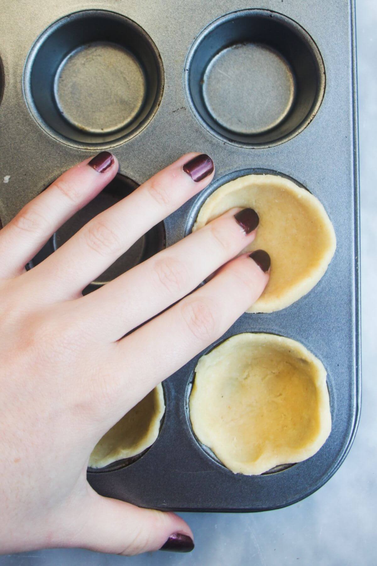 Hand pressing pastry circles into a small muffin tin.